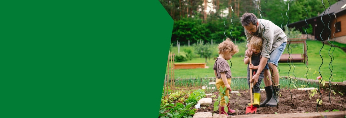 Eine Person und zwei Kinder bei der Gartenarbeit mit einer Schaufel.